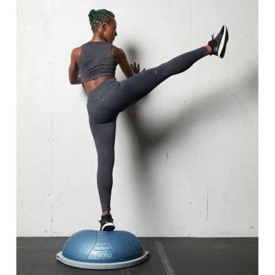 Individual holding a wall for support while doing single-leg balance swings on BOSU