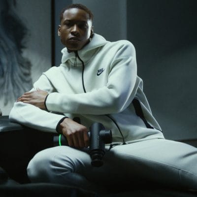 Athlete sitting and holding a Hyperice Hypervolt massage gun as part of his warm-up or recovery routine.