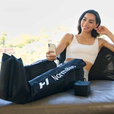 Woman relaxing on couch using Normatec 3 Legs compression boots for post-workout recovery and circulation improvement