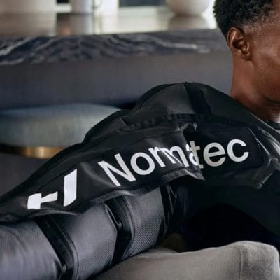 Person using Hyperice Normatec arm attachments connected to a Normatec control unit