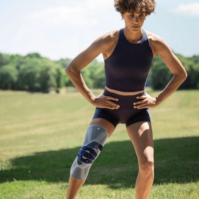 Athlete wearing the titan and blue Bauerfeind GenuTrain P3 knee brace with grip top on the field
